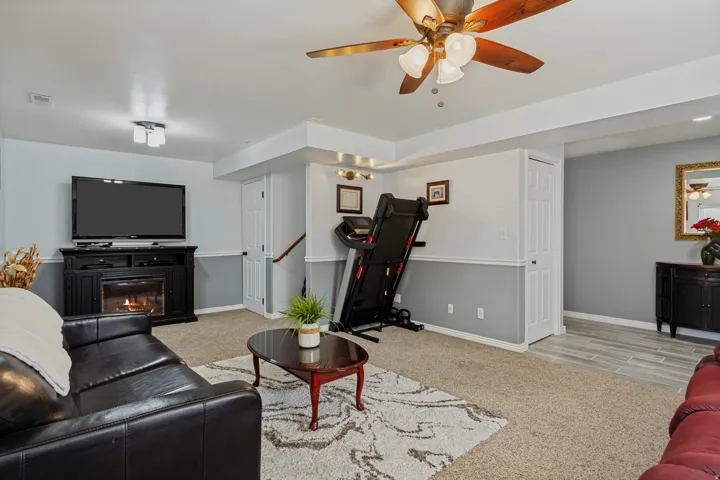 Recessed ceiling with integrated lighting, wood-finish ceiling fan, built-in fireplace with mantle, wall-mounted television, and two-tone wall treatment