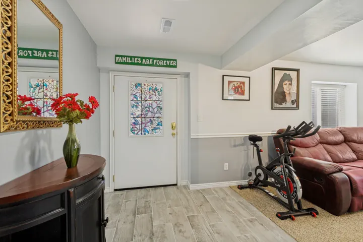 Welcoming entryway with wood-finish flooring, ornate gold-framed mirror, decorative tile-inset door, and green signage accent