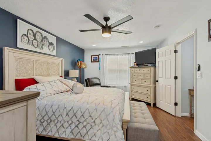 Spacious primary bedroom featuring a wood-finish accent wall, ceiling fan with integrated lighting, wood-finish dresser with ample storage, and hardwood flooring throughout
