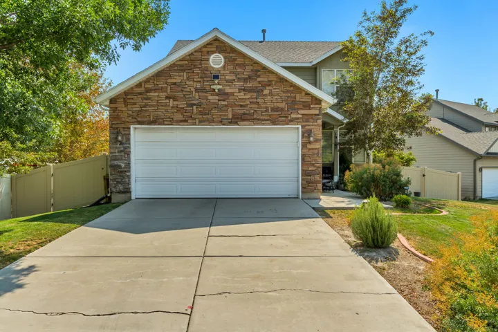 Stone facade with an attached garage, featuring a concrete driveway, and surrounding green landscaping