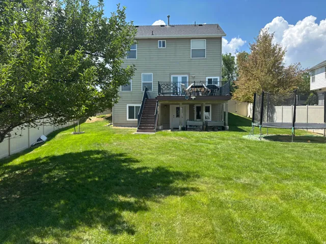 Spacious backyard featuring a manicured lawn, full privacy fencing, mature trees, a multi-level deck, and a lower-level walk-out