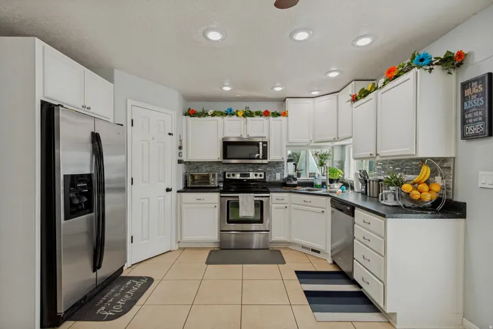 White cabinetry with stainless steel appliances, dark countertops, and tile flooring