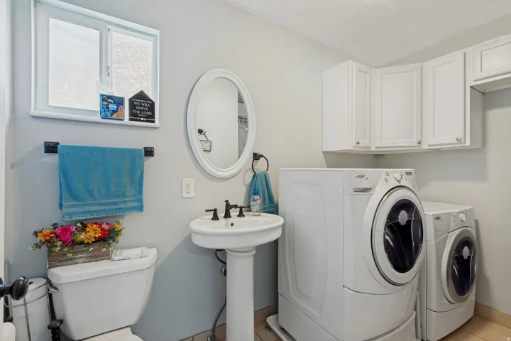 Pedestal sink, white pedestal toilet, white overhead cabinetry, and a window providing natural illumination