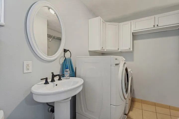 Pedestal sink with dark-toned fixtures, ceramic tile flooring, and white upper cabinetry