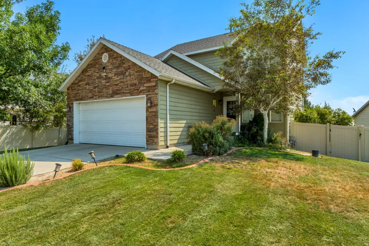 Exterior featuring stone accents, horizontal siding, an attached garage, a paved driveway, and landscaping with mature trees
