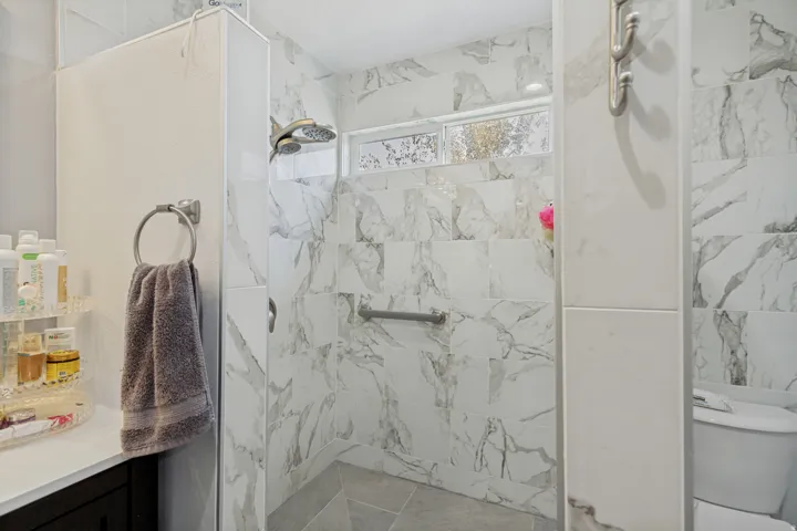 Walk-in shower with marble-look tile, rainfall showerhead, and window