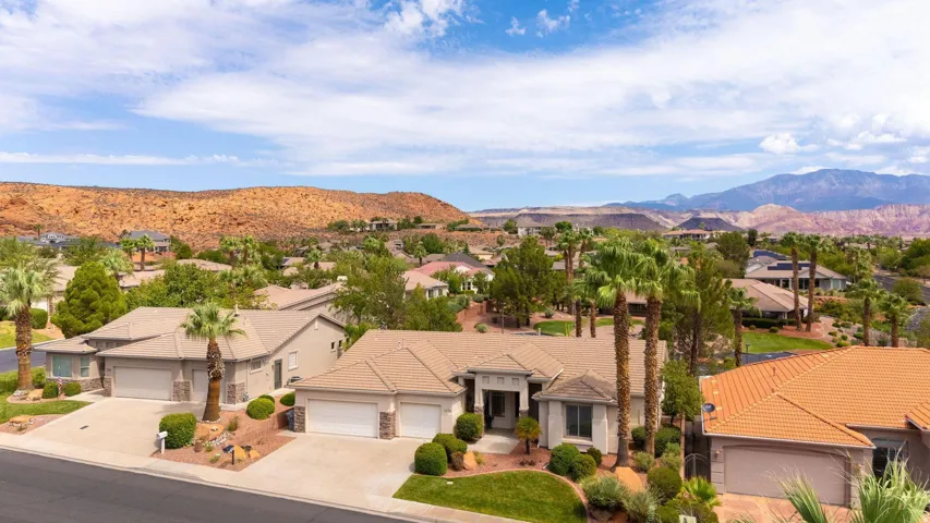 Single-story residence featuring a neutral exterior, multi-car garage, and a manicured front landscape with mature palm trees