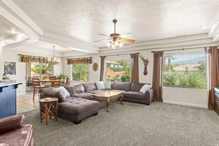 Expansive living space featuring tray ceilings with recessed lighting and a ceiling fan