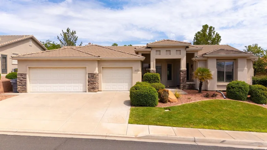 Stucco exterior home featuring a tile roof, an integrated two-car garage with individual doors, a paved driveway, and a landscaped front yard with grass and decorative rock