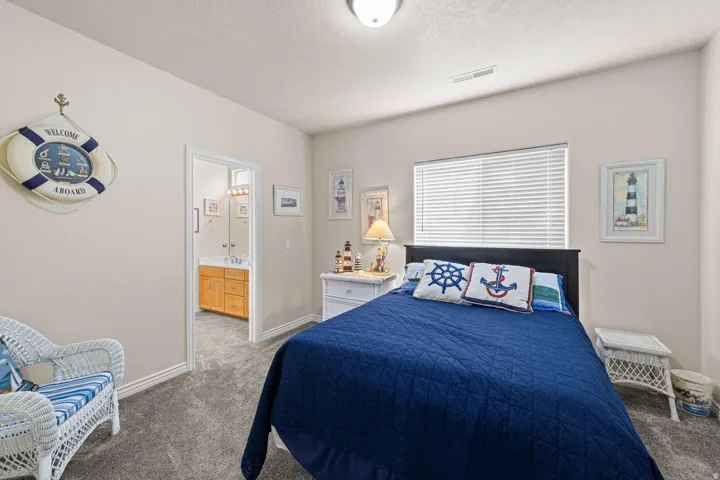 Neutral-toned bedroom featuring wall-to-wall carpeting, a window with horizontal blinds, and an entryway to a full bathroom