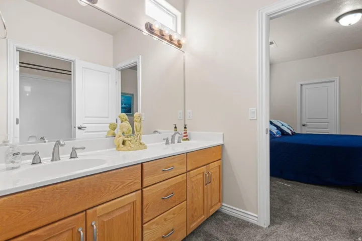 Bathroom vanity featuring dual sinks with individual faucets, ample storage cabinetry with wood-finish doors and drawers, and an expansive mirror