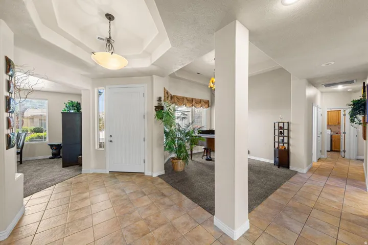 Foyer featuring ceramic tile flooring, a tray ceiling with a hanging light fixture, and a white paneled entry door with a sidelight