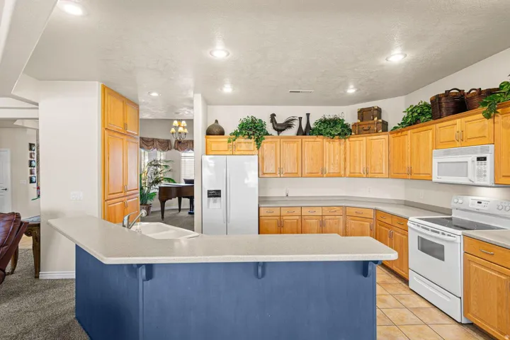 Kitchen featuring light wood-finish cabinetry, white appliances, and a blue-painted island with an integrated sink