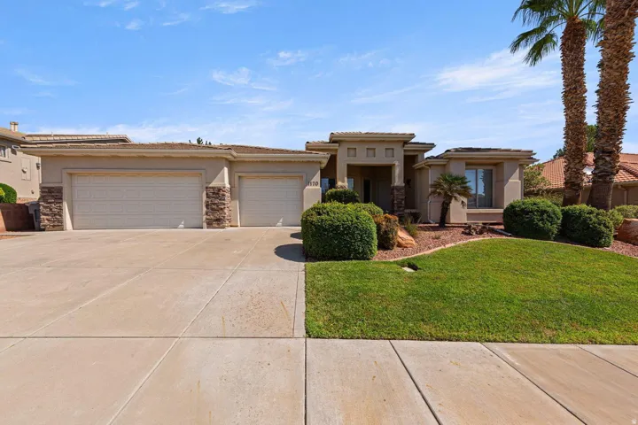 Stucco exterior with stone accents, mature landscaping, concrete driveway, and attached two-car garage