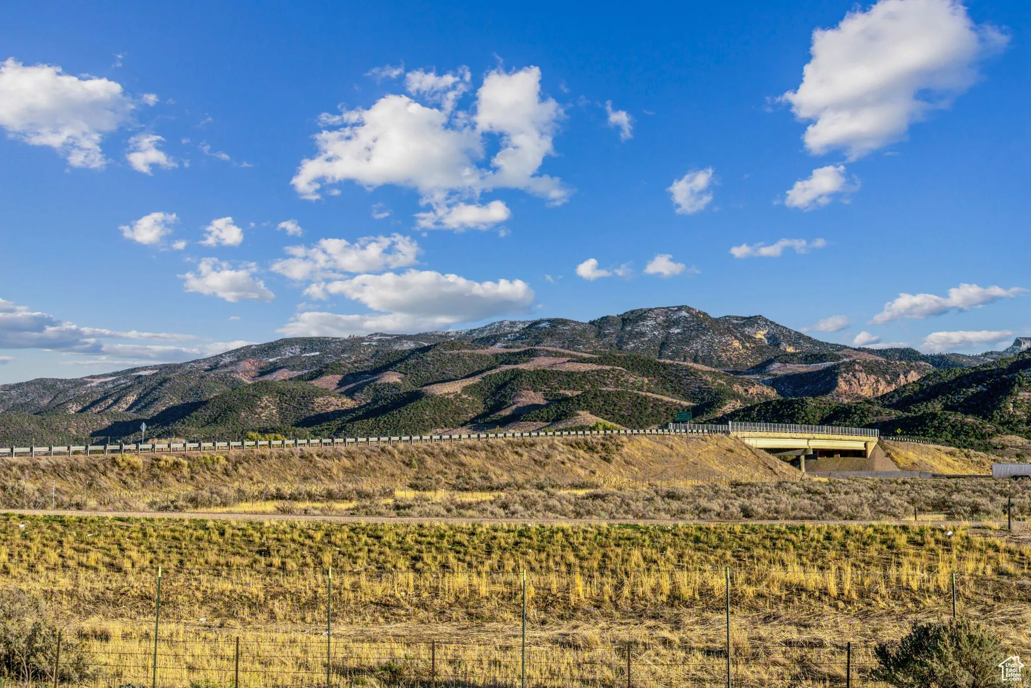 Expansive mountain landscape with a clear blue sky, featuring a modern highway overpass