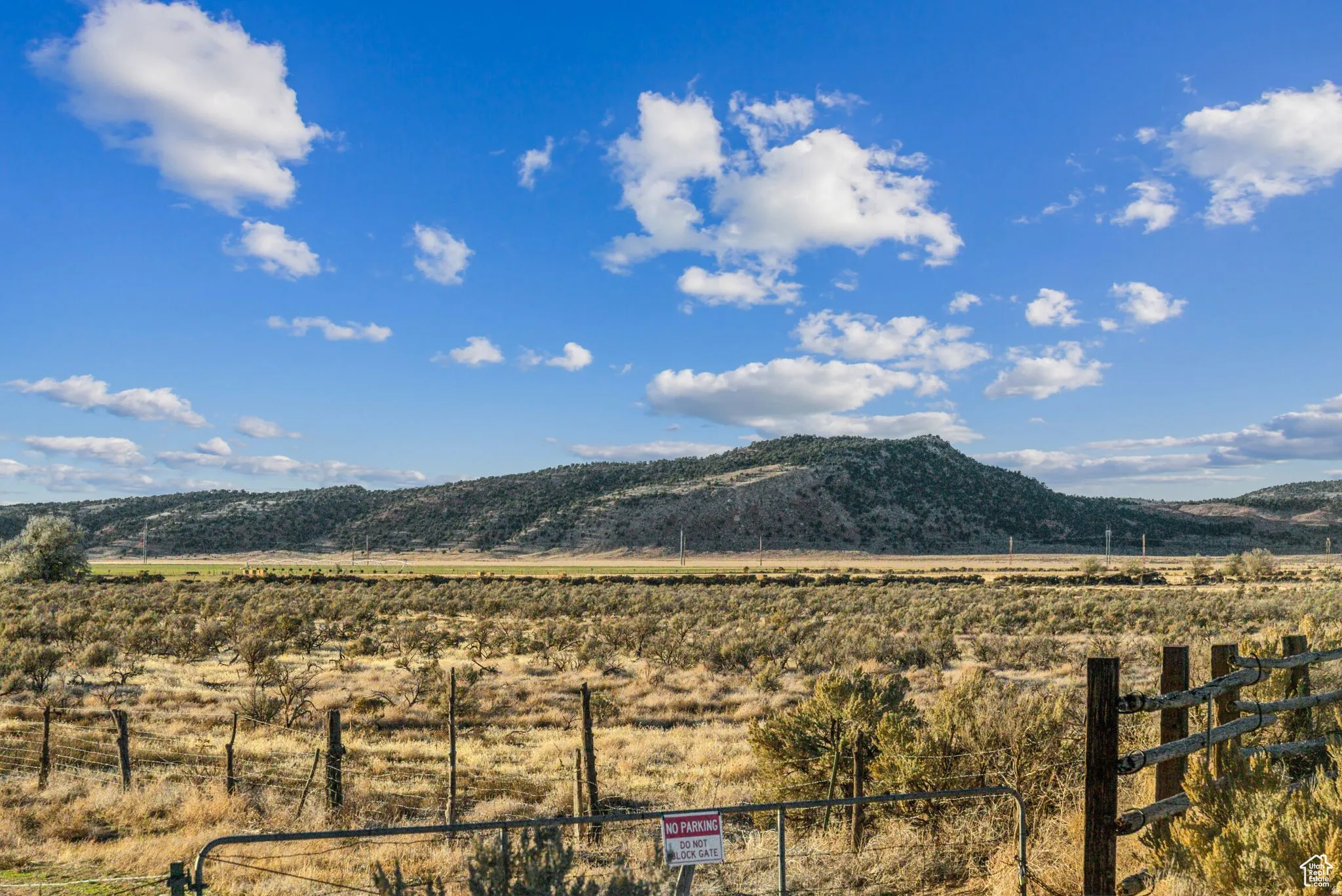 Expansive open land with distant hills, a clear sky, and a rustic perimeter fence