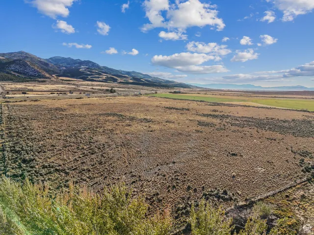 Expansive undeveloped land featuring varied terrain, distant mountains, a partially cultivated field, and a clear blue sky with clouds