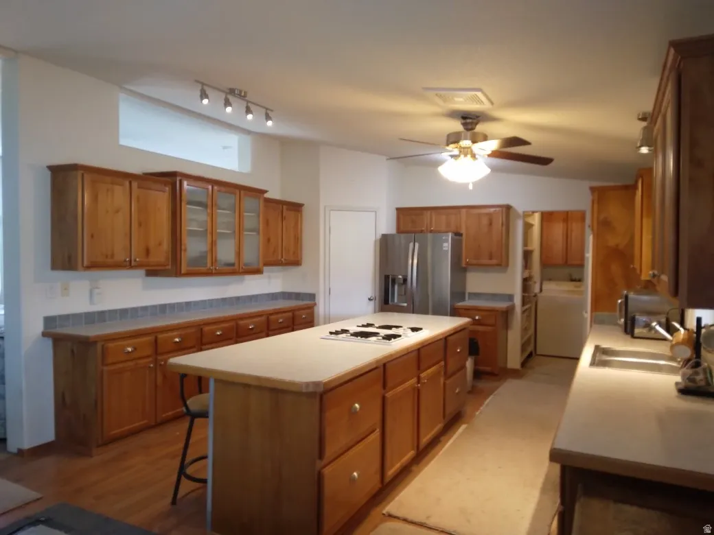 Expansive kitchen featuring wood cabinetry, a central island with an integrated cooktop, stainless steel refrigerator, and recessed lighting