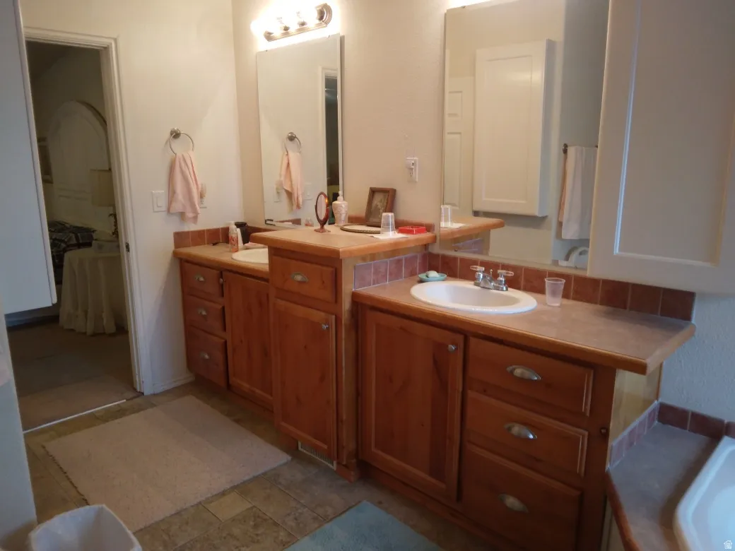 Dual vanity with wood-finish cabinetry, integrated sinks, and tiled backsplashes