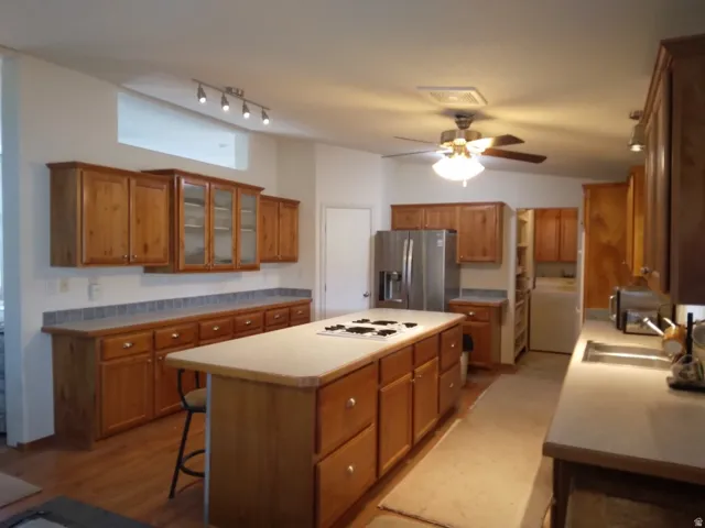 Expansive kitchen featuring wood cabinetry, a central island with an integrated cooktop, stainless steel refrigerator, and recessed lighting