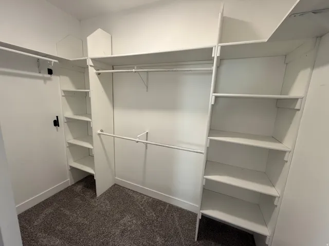 Walk-in closet featuring white built-in shelving, multiple hanging rods, and neutral-toned carpeting