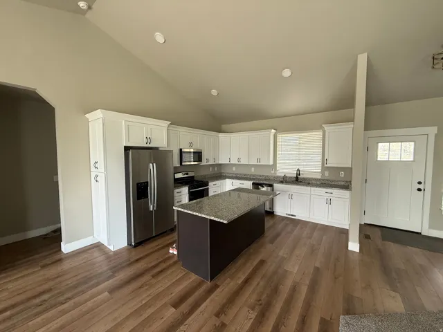 Spacious kitchen featuring white cabinetry, stainless steel appliances, granite countertops, and LVP wood-finish flooring