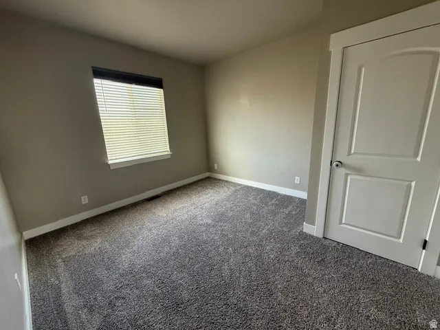 Neutral-toned room featuring a single window with horizontal blinds, light tan walls, and textured grey carpeting