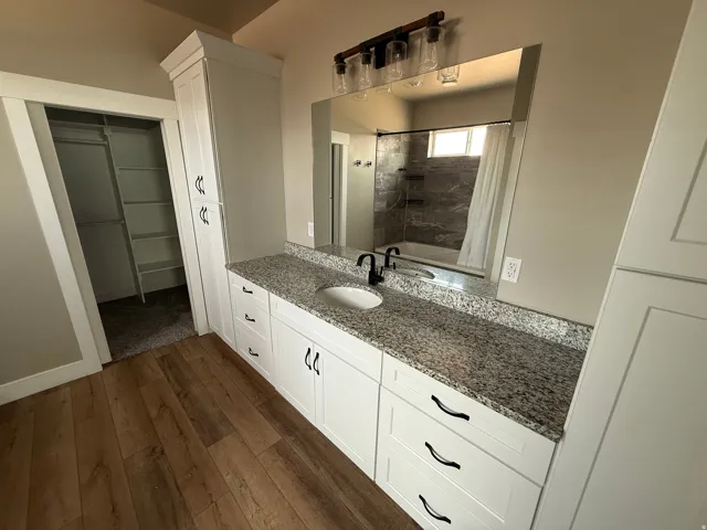 Bathroom featuring a double vanity with granite countertop, white cabinetry with black hardware, and wood-finish flooring