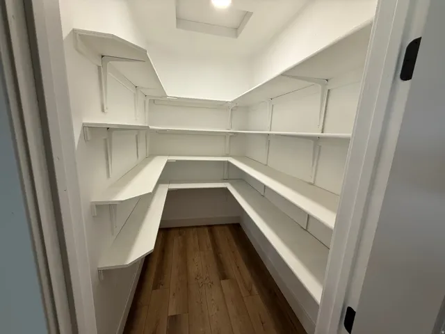 Walk-in pantry featuring white shelving, wood-finish flooring, and recessed ceiling lighting