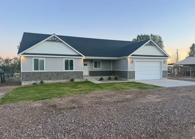 Contemporary ranch-style home featuring light gray siding with a stone veneer accent, a dark asphalt shingle roof, a white front door, and an attached two-car garage with a white panel door
