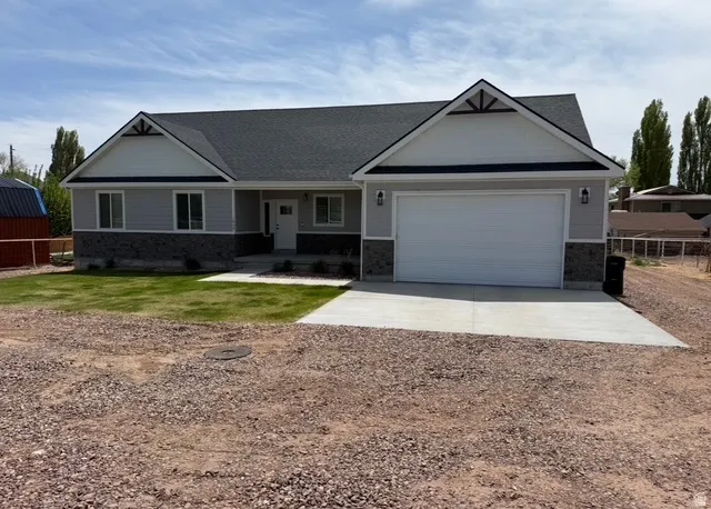 Single-story residence featuring light gray siding with dark stone wainscoting, a dark shingle roof, and a two-car garage