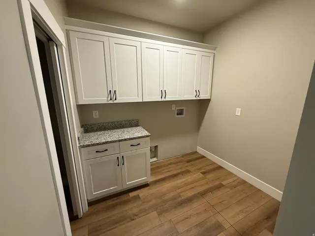 Utility room featuring white shaker cabinetry with black hardware, a speckled countertop, and wood-finish flooring