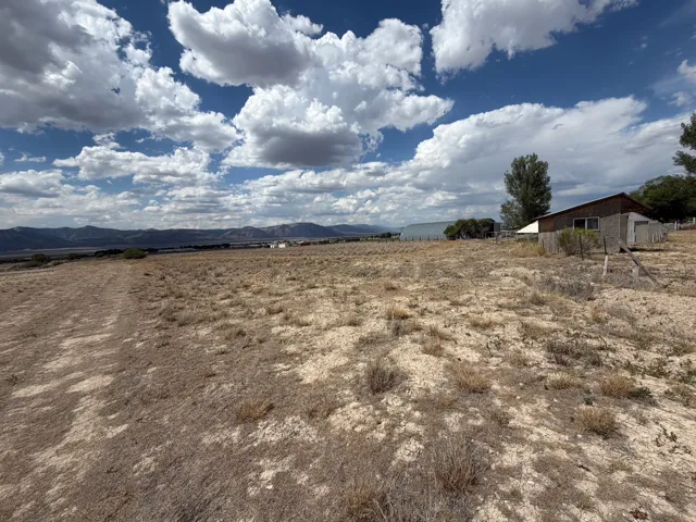 Expansive land featuring a distant mountain range, a metal-sided outbuilding, a wood-sided structure with a gray base, and mature trees