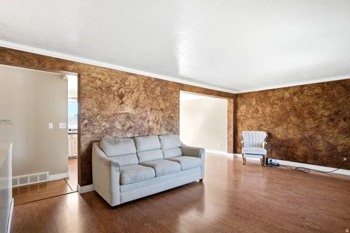 Spacious interior featuring patterned accent walls, rich wood-finish flooring, white crown molding, and an arched doorway