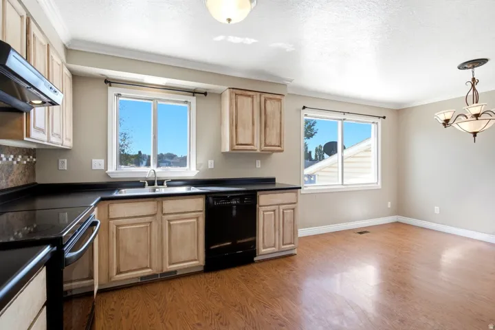 Kitchen and dining area featuring wood-finish flooring, two large windows, black appliances, light wood cabinetry, and a decorative chandelier