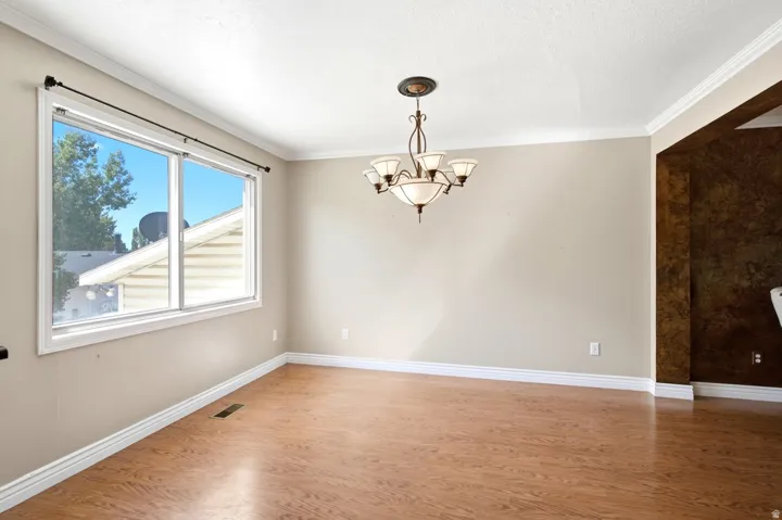 Spacious room with wood-finish flooring, white baseboards, and crown molding