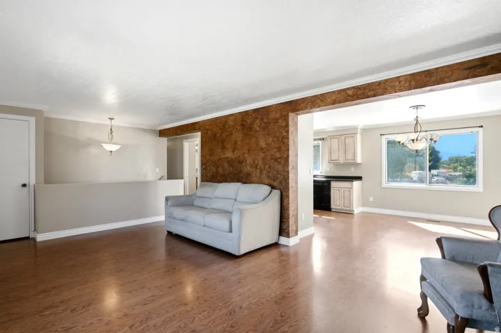 Open-concept living area featuring wood-finish flooring, textured accent wall, and recessed kitchen with light cabinetry