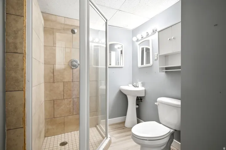 Tiled shower enclosure with glass surround, pedestal sink, and white vanity cabinet with shelving