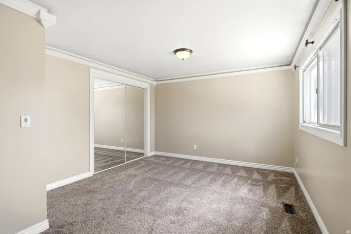 Spacious interior room featuring neutral-toned walls, crown molding, and plush patterned carpeting