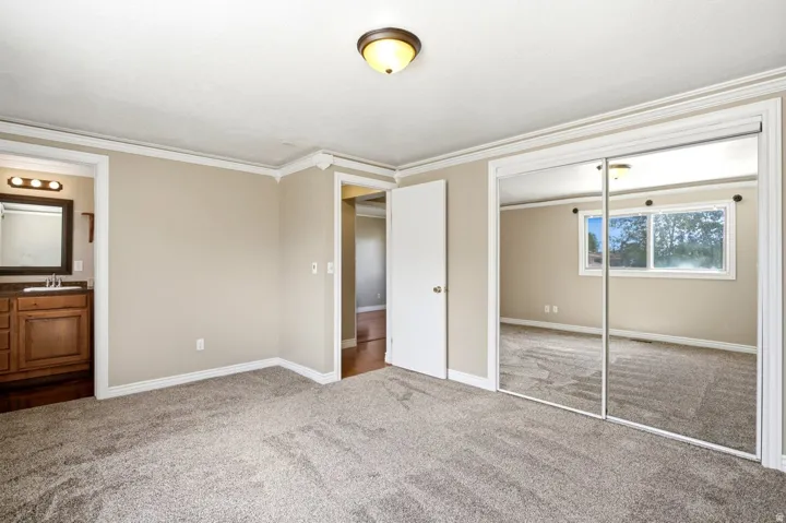 Carpeted room featuring crown molding, neutral wall paint, and mirrored closet doors