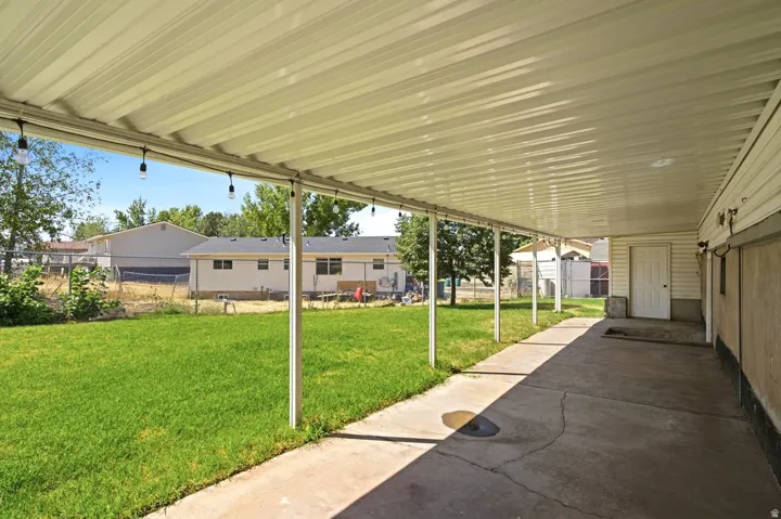 Covered concrete patio with string lights extending to a verdant lawn
