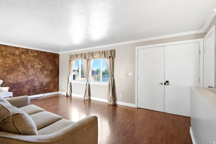 Living area featuring wood-finish flooring, a textured accent wall, multiple windows with natural light, and crown molding