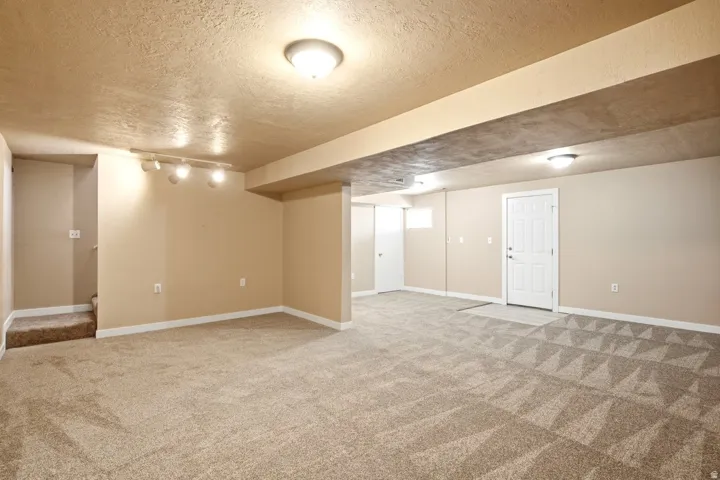 Expansive carpeted area featuring recessed lighting, a track light fixture, and a solid-core door