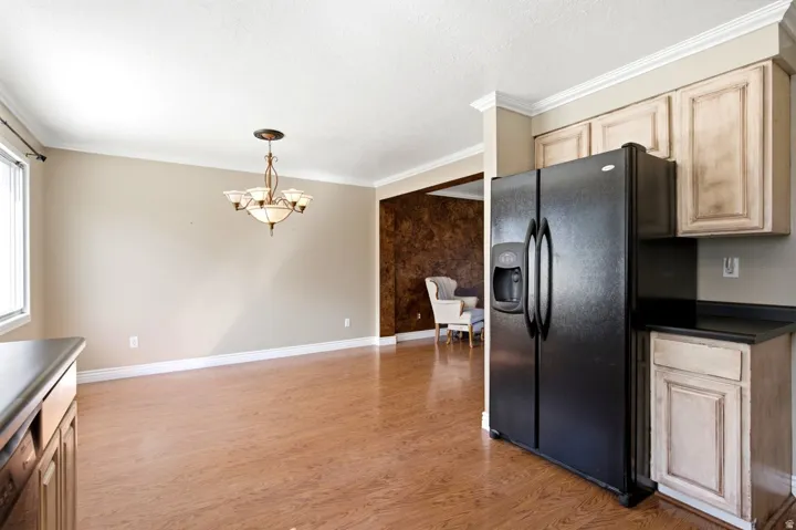 Open-concept interior featuring wood-finish flooring, a traditional chandelier, crown molding, and a built-in black refrigerator
