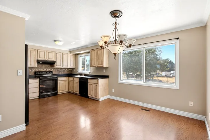 Kitchen and dining area featuring wood-finish flooring, light-toned cabinetry, dark countertops, and a black appliance suite including a range, dishwasher, and refrigerator
