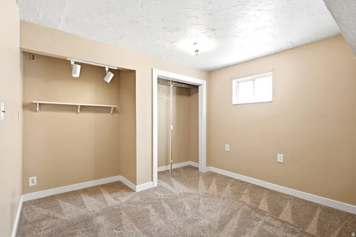 Room featuring light tan walls, textured ceiling, a window, and track lighting over a built-in shelf