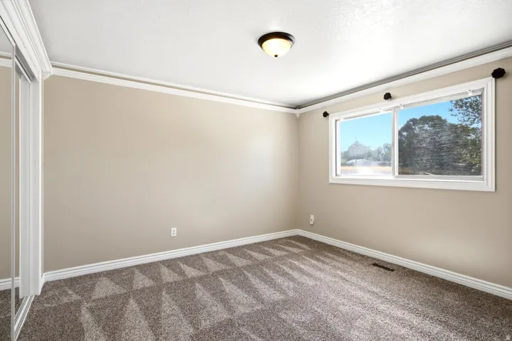 Carpeted room featuring a double-pane window, mirrored closet doors, and crown molding