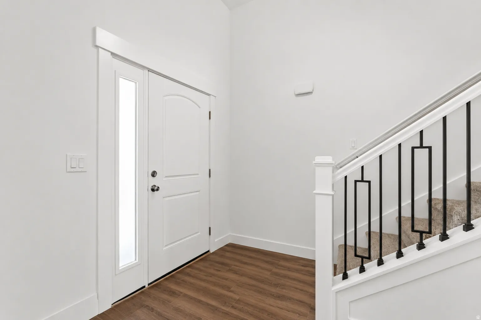 Entryway featuring wood-finish flooring, a white door with an arched panel, a full-length sidelight, and a staircase with black metal balusters and a white handrail