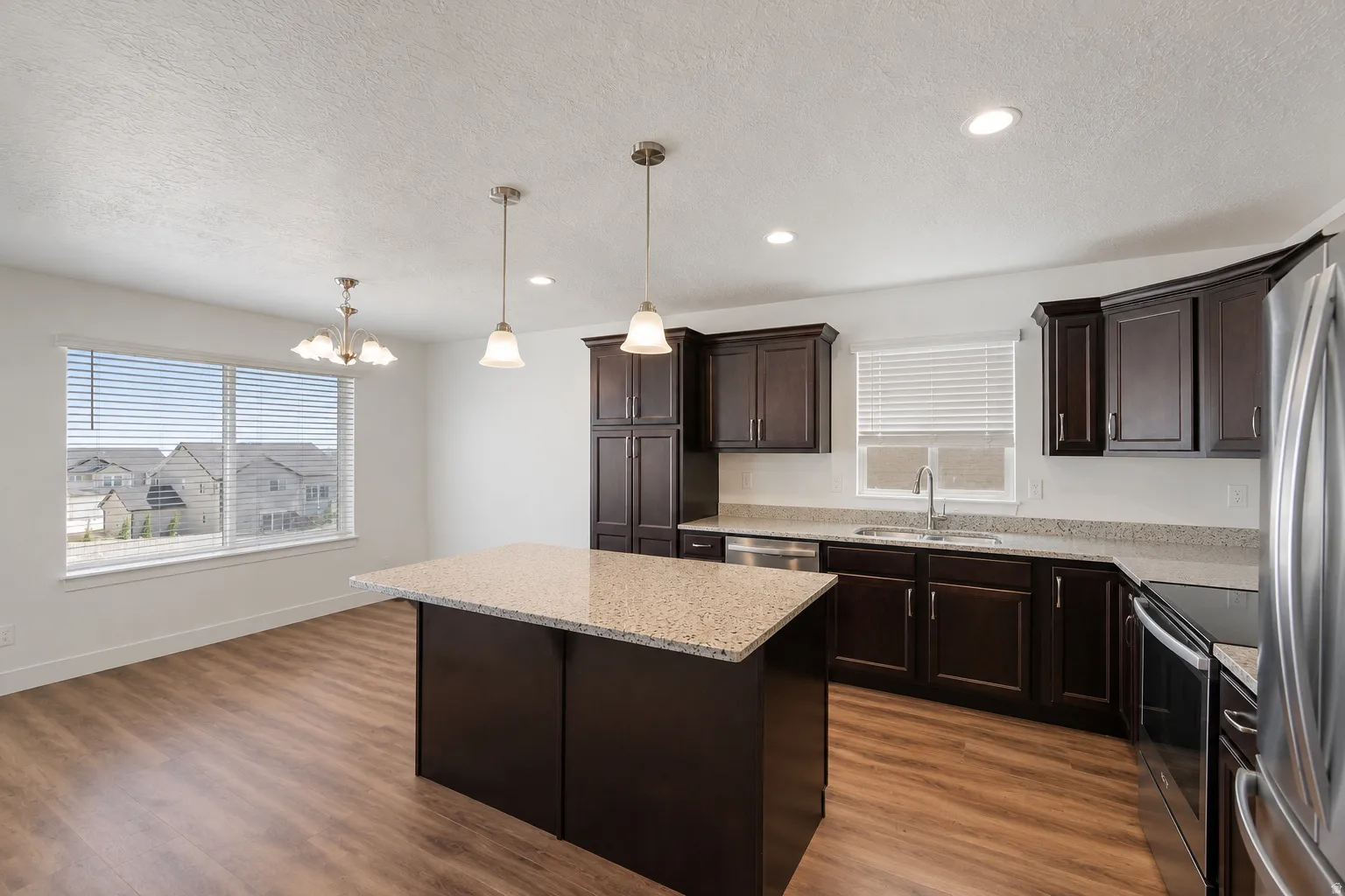 Open-concept kitchen and dining area featuring a central island with granite countertop, dark wood-finish cabinetry, stainless steel appliances, and wood-finish flooring