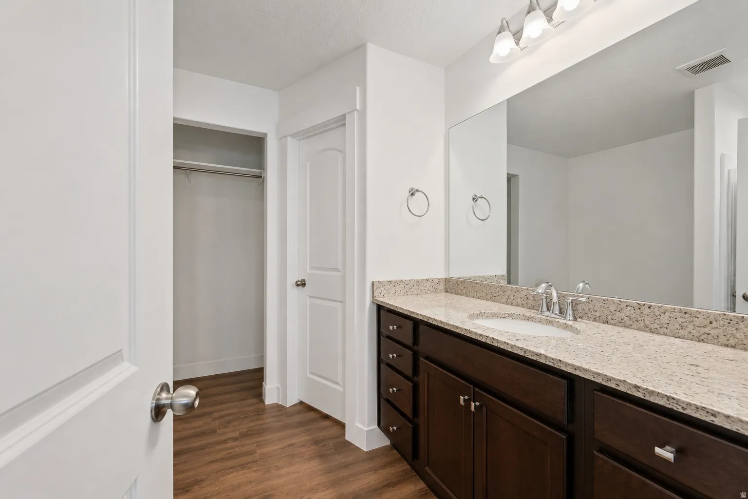 Bathroom vanity featuring a light-toned countertop, an undermount sink with a chrome faucet, and dark wood-finish cabinetry